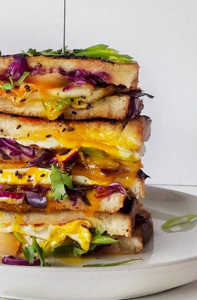 This kimchi grilled cheese breakfast sandwich features a sesame seed crust with mango habanero cheddar cheese, red cabbage, cilantro, scallions, green onions, fried egg sandwich. half baked harvest, bibimbap, korean food, korean fusion, sourdough bread, fancy grilled cheese, brunch,