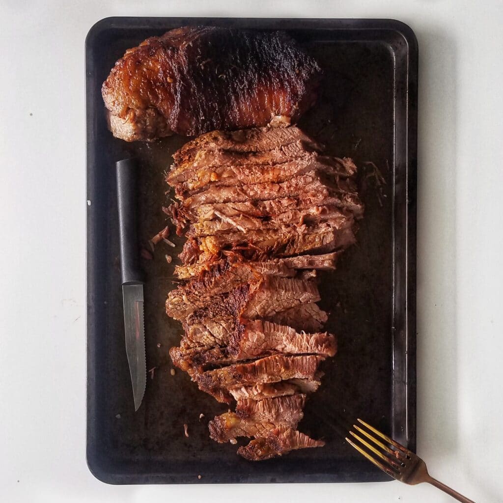 brisket on baking sheet with knife and fork for brisket sandwich recipe found on mandyolive.com