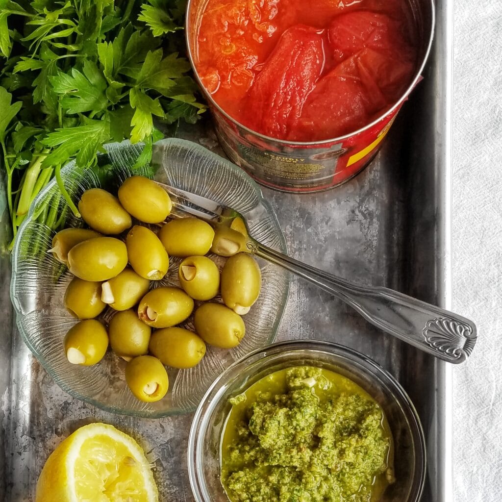 puttanesca sauce ingredients: whole tomatoes, olive tapenade, and garlic stuffed olives. Cheaters puttanesca recipe found on mandyolive.com