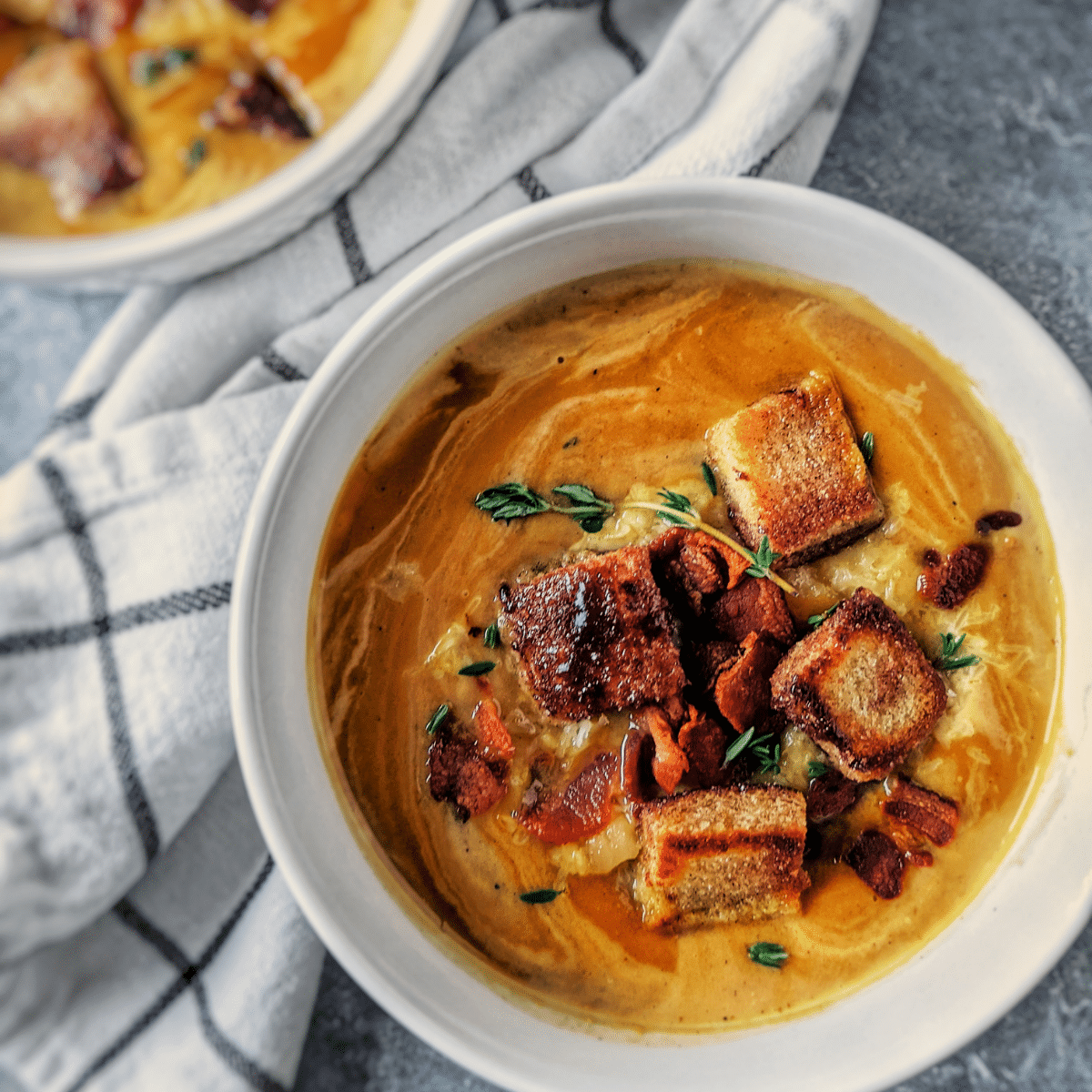 smoky pumpkin and butternut squash soup in bowls topped with gouda cheese, cinnamon sugar croutons and fresh herbs. Full recipe found on mandyolive.com