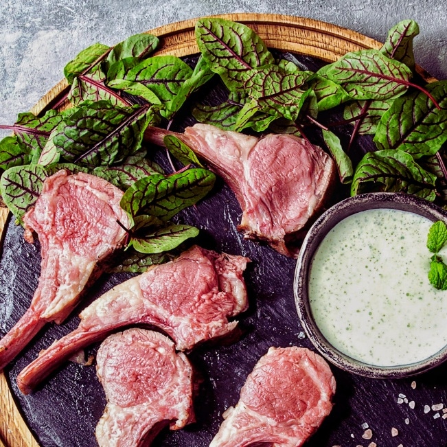 herb crusted lamb on plate with greens and yogurt sauce