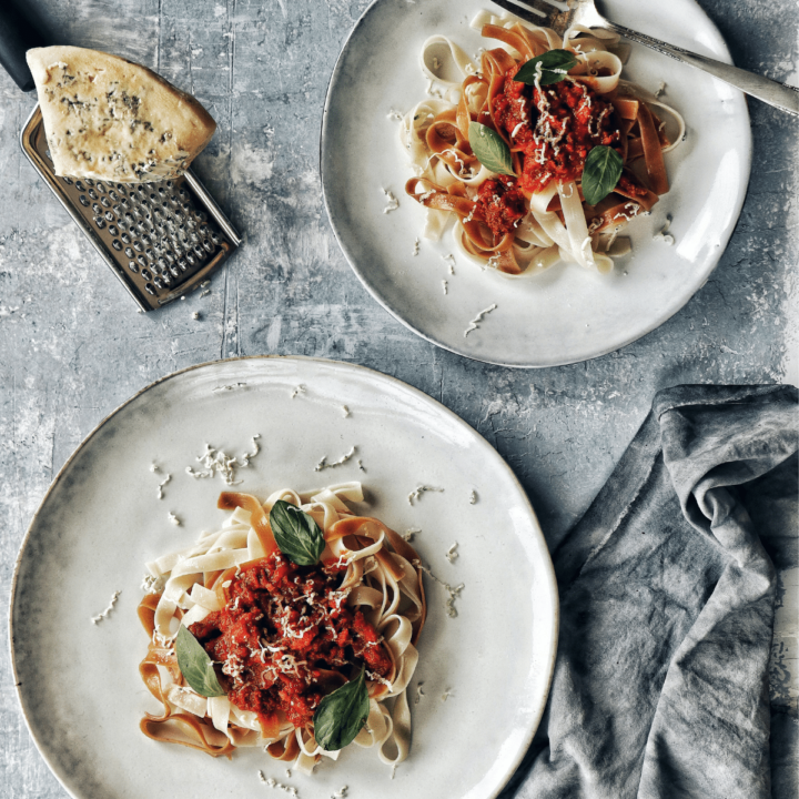 Red pepper pasta sauce over pasta with parmesan cheese block in the top left corner