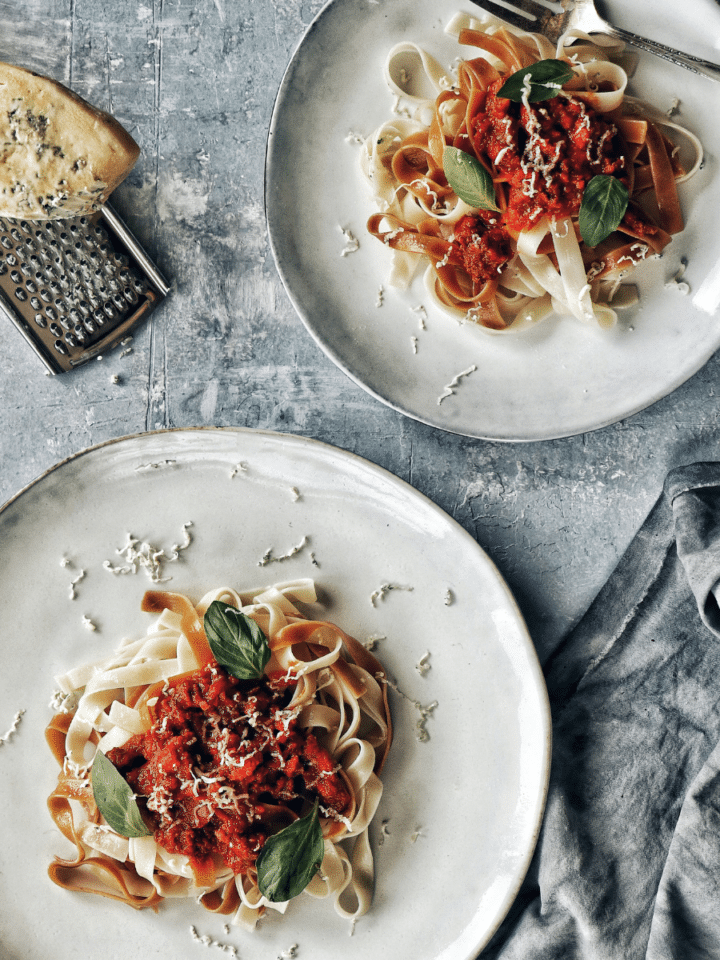 Red pepper pasta sauce over pasta with parmesan cheese block in the top left corner